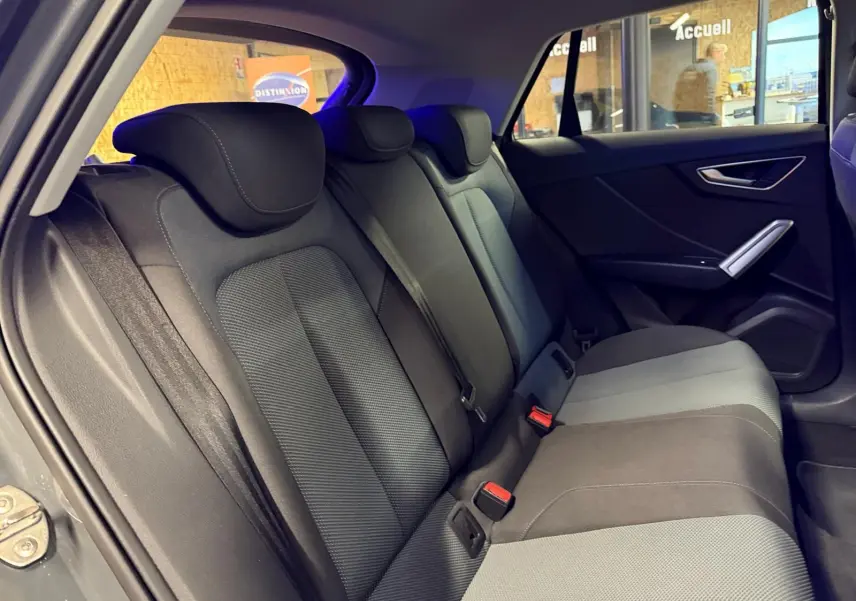 Vue intérieure côté droit montrant la banquette arrière gris foncé et clair de l'Audi Q2 avec appuie-têtes et ceintures de sécurité.