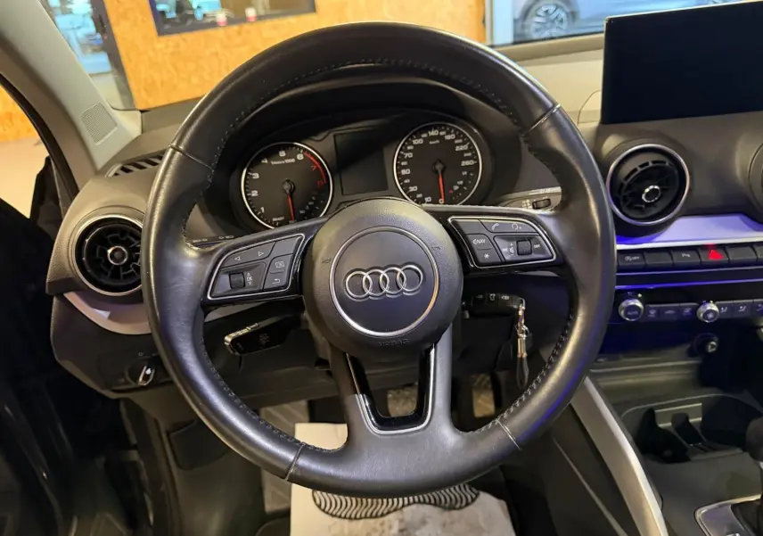Vue intérieure centrée sur le volant cuir multifonctions noir de l'Audi Q2 avec tableau de bord et écran multifonction.