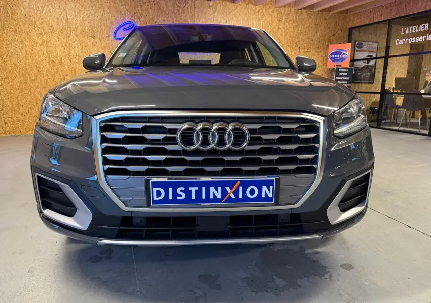 Vue frontale d'un Audi Q2 gris avec calandre hexagonale et détails chromés, en intérieur d'atelier.
