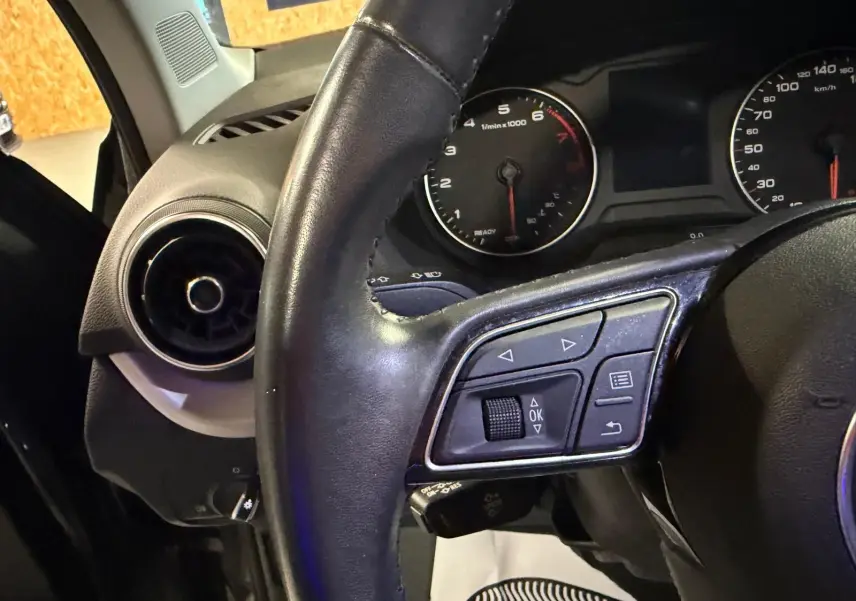 Gros plan sur le volant cuir et le tableau de bord noir de l'Audi Q2, avec commandes multifonctions visibles.