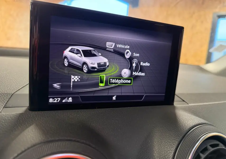 Écran multimédia intérieur montrant un Audi Q2 gris en vue 3/4 avant avec menu de contrôle tactile.