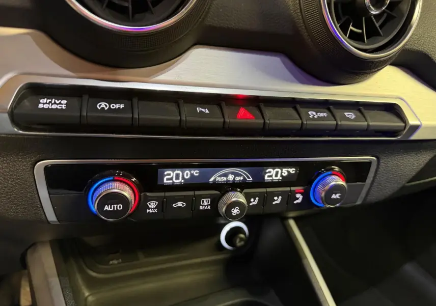 Gros plan sur la console centrale de l'Audi Q2 gris, montrant les commandes de climatisation automatique et les boutons de fonction.