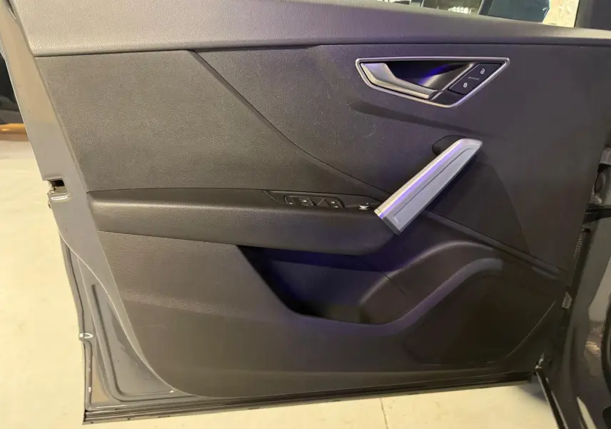 Vue rapprochée de la porte avant gauche de l'Audi Q2 gris, avec commandes électriques et poignée argentée.