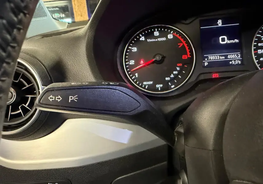 Gros plan sur le commodo gauche du tableau de bord de l'Audi Q2 gris, avec compte-tours et écran multifonction en arrière-plan.