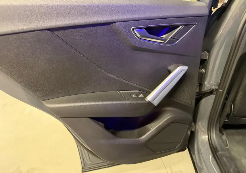 Vue rapprochée de la porte arrière droite gris foncé de l'Audi Q2 avec poignée argentée et bouton de vitre électrique.