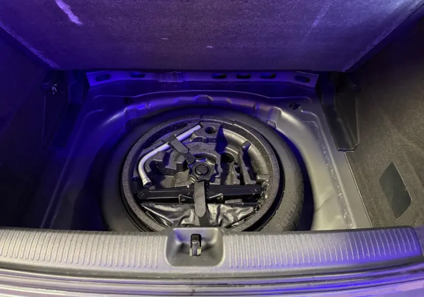 Vue plongeante sur la roue de secours et les outils dans le coffre d'un Audi Q2 gris 2018.