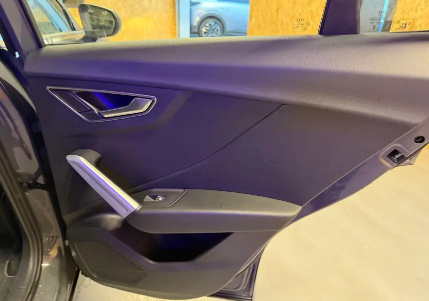 Vue intérieure de la porte arrière gauche gris foncé de l'Audi Q2 avec poignée argentée et commande de vitre électrique.