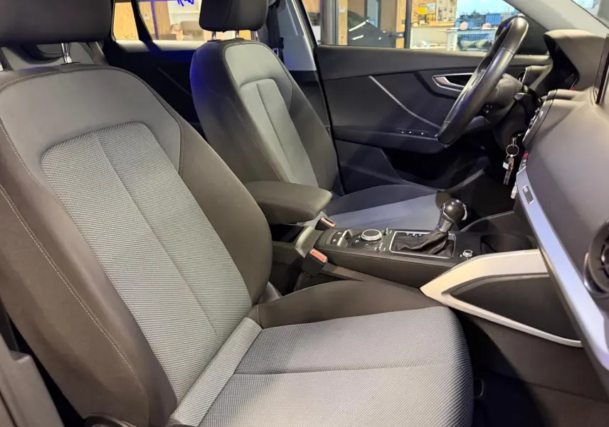Vue intérieure côté conducteur de l'Audi Q2 2018, sièges tissu gris et console centrale avec levier de vitesse.