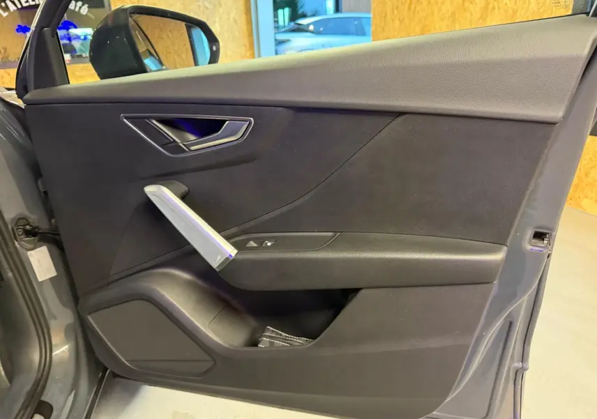 Vue intérieure de la porte avant gauche gris foncé de l'Audi Q2 avec poignée argentée et commandes électriques.