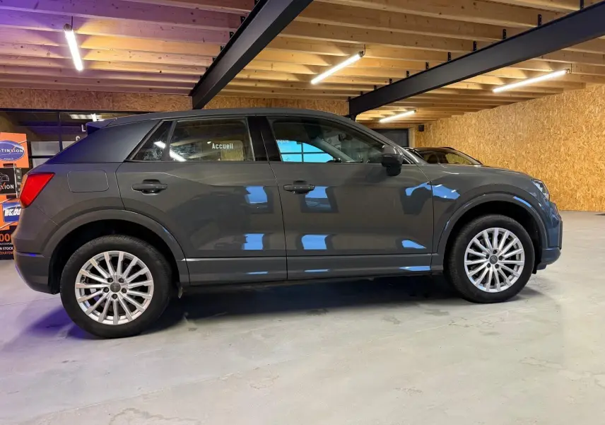 Audi Q2 gris vue de profil côté gauche dans un garage, avec jantes alliage et rétroviseurs noirs.