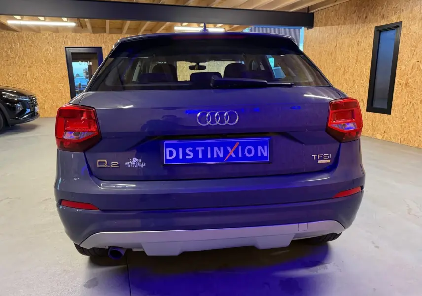 Vue arrière d'un Audi Q2 gris avec feux rouges, logo TFSI et plaque Distinxion dans un garage.