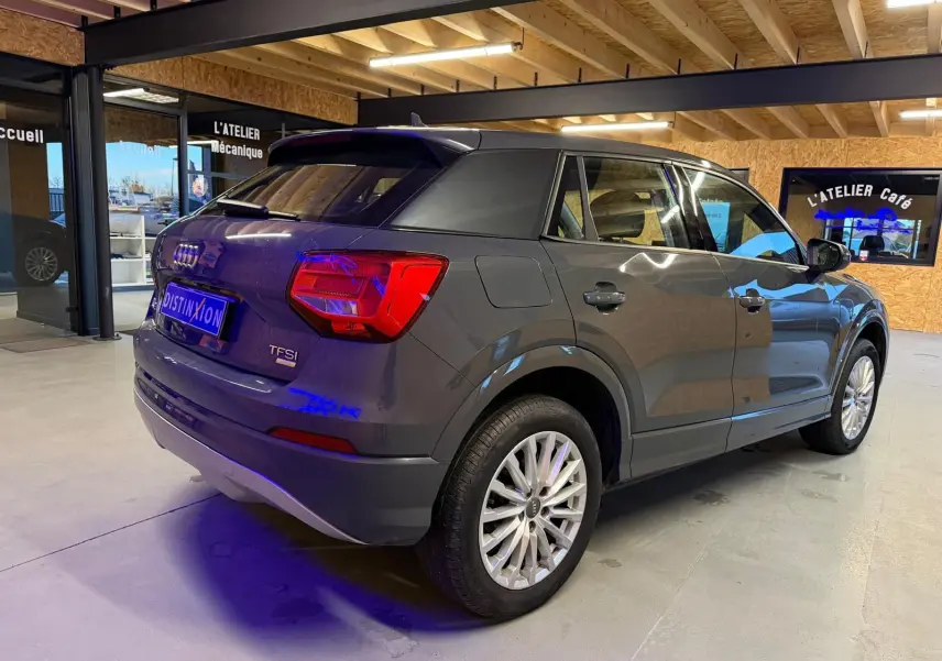 Audi Q2 gris vue 3/4 arrière droit en intérieur, avec jantes alu et feux arrière LED visibles.
