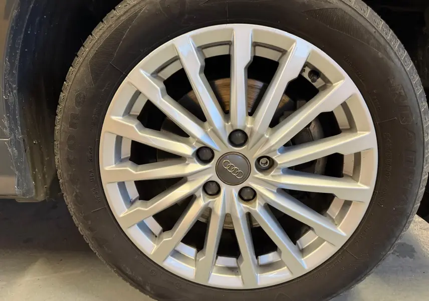 Gros plan sur la jante alu argentée d’un Audi Q2 gris, mettant en valeur le logo Audi au centre.