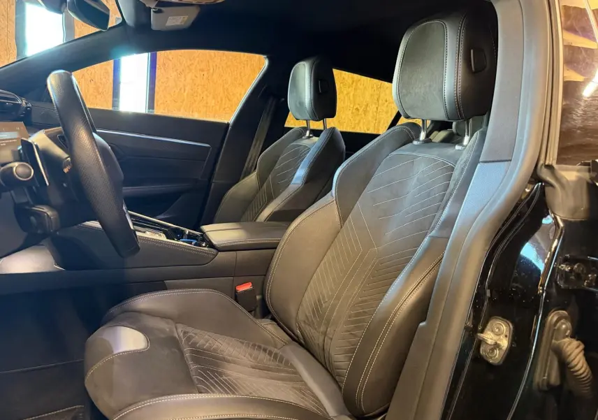 Vue intérieure côté conducteur de la Peugeot 508 SW 2024, sièges Alcantara noirs avec surpiqûres Aïkinite et volant cuir perforé.