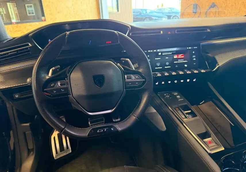 Vue intérieure du poste de conduite du Peugeot 508 SW GT 2024, volant cuir perforé avec badge GT et tableau de bord numérique.