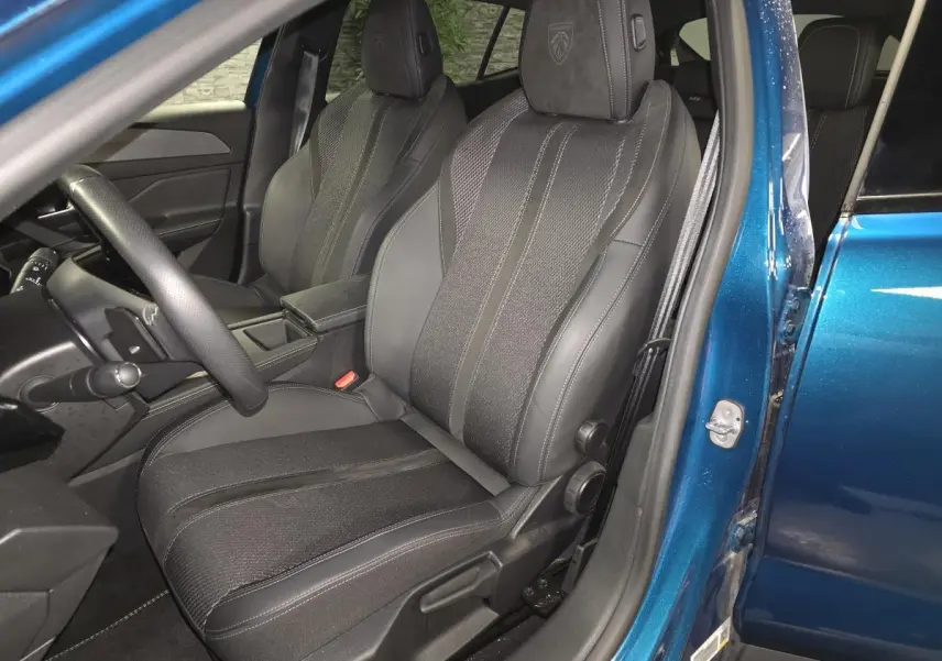Vue intérieure côté conducteur du siège avant en tissu et cuir noir de la Peugeot 408 bleu 2024, avec appui-tête embossé Lion.