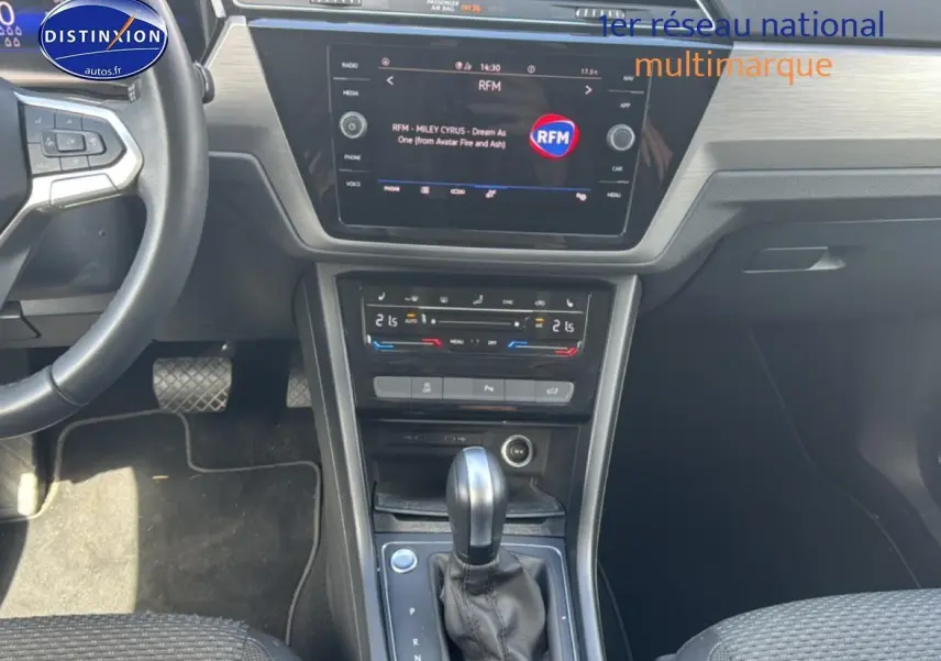 Vue intérieure centrée sur la console centrale et levier de vitesse d’un Volkswagen Touran noir, avec écran tactile et climatisation tri-zone.