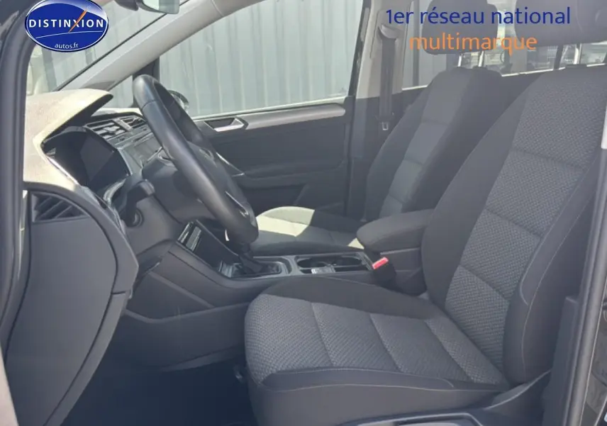 Vue intérieure côté conducteur du Volkswagen Touran 2025, sièges tissu gris et volant cuir multifonction.