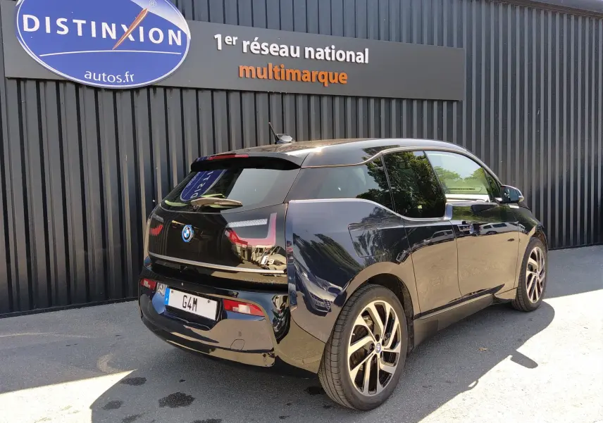 Vue 3/4 arrière droite d'une BMW i3 noire électrique garée devant un mur avec un panneau Distinxion.