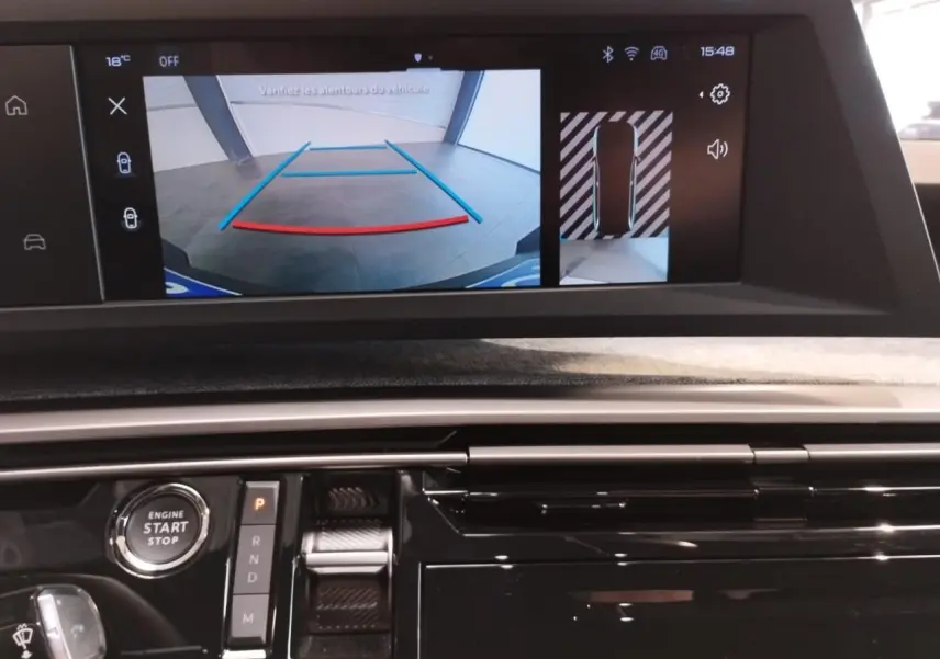 Vue intérieure du tableau de bord du Peugeot 5008 Hybrid 2025, écran de caméra de recul et commandes de boîte auto visibles.