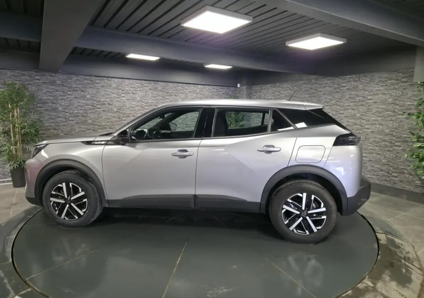 Peugeot 2008 gris en profil droit, jantes noires et argent, toit noir contrastant, dans un showroom intérieur.