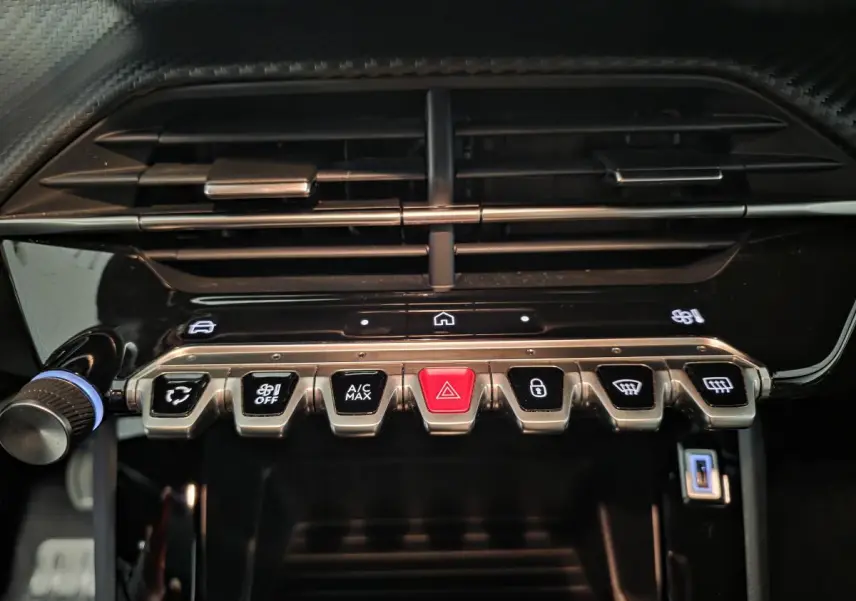 Gros plan sur la console centrale de la Peugeot 2008 2025, boutons métalliques et finition noire brillante.