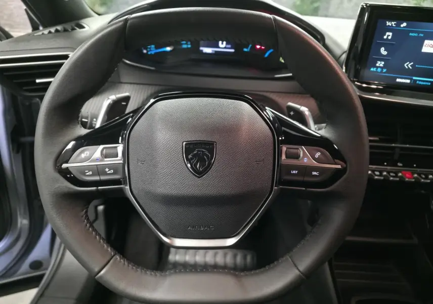 Vue rapprochée du volant cuir noir avec commandes intégrées du Peugeot 2008 gris, tableau de bord et écran tactile visibles.