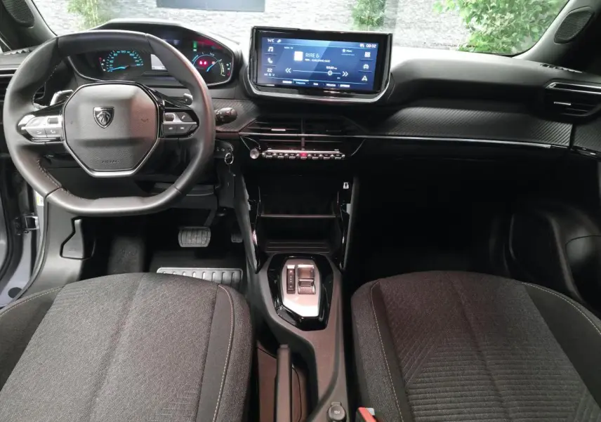 Vue intérieure avant du Peugeot 2008 gris 2025, tableau de bord carbone, écran tactile 10 pouces et volant compact cuir.