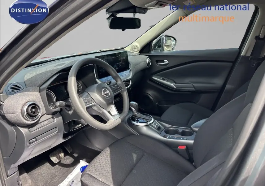 Vue intérieure côté conducteur du Nissan Juke Hybrid 2024, avec tableau de bord moderne et sièges tissu noir.