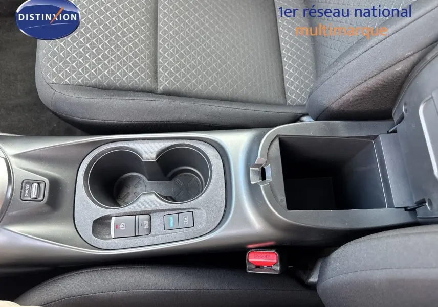 Vue plongeante sur la console centrale du Nissan Juke Hybrid 2024, avec porte-gobelets et accoudoir ouvert en tissu noir.