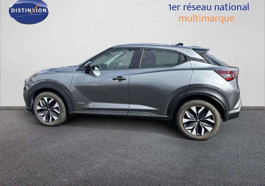 Nissan Juke Hybrid gris squale métal vu de profil côté gauche, avec jantes alliage et lignes dynamiques marquées.