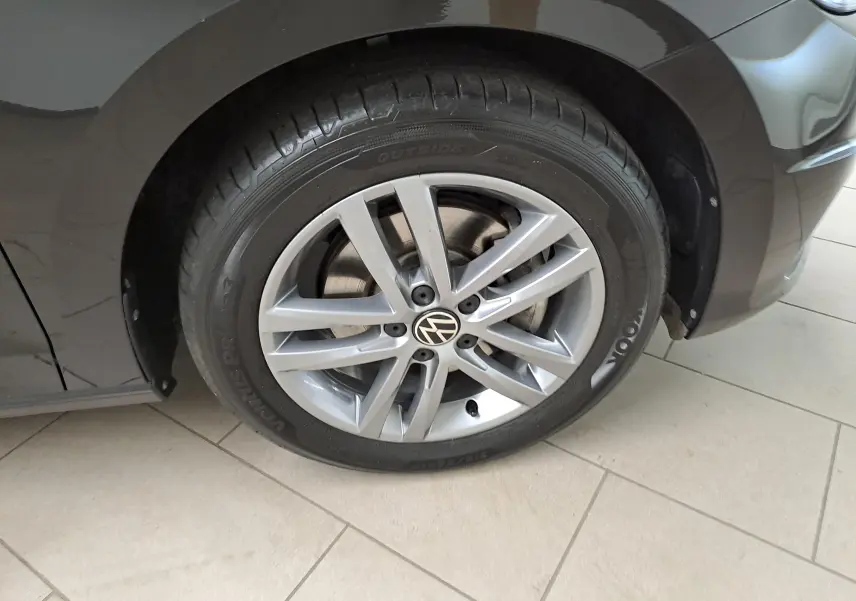 Gros plan sur la roue avant gauche du Volkswagen Touran noir grenadille, mettant en valeur la jante alliage argentée et le logo VW.