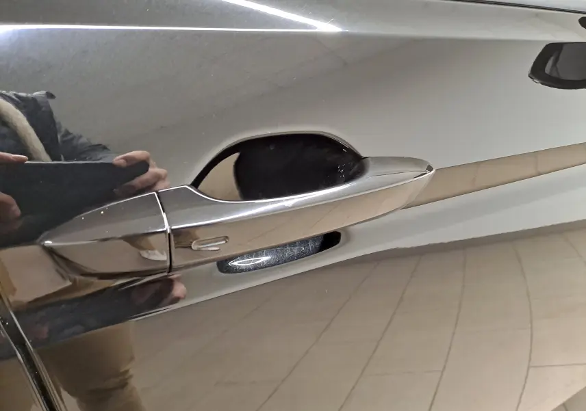 Poignée de porte chromée côté gauche sur Volkswagen Touran Noir Grenadille avec reflet du sol carrelé intérieur.