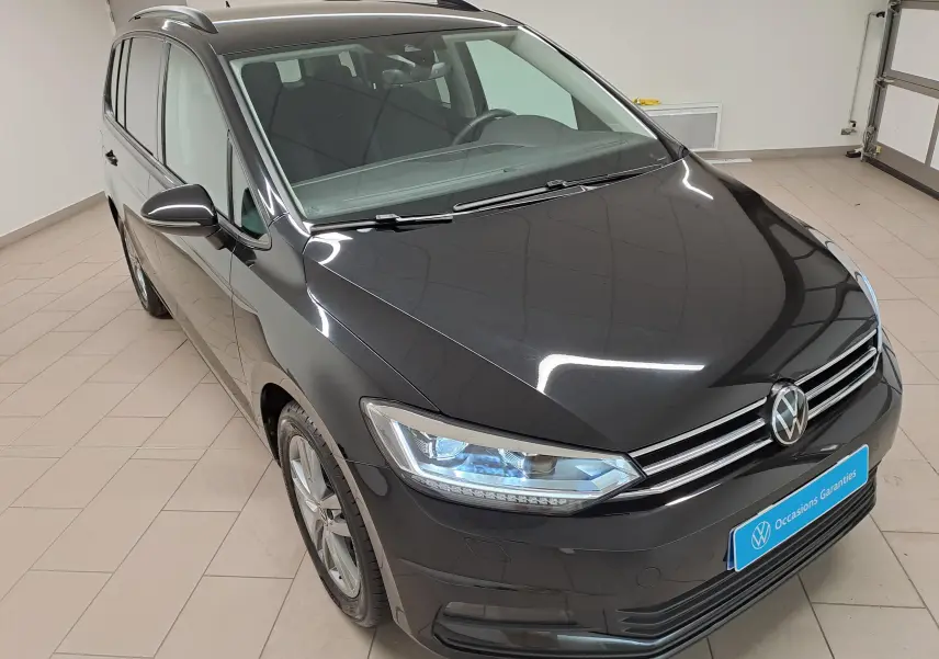 Vue 3/4 avant gauche d’un Volkswagen Touran noir grenadille métallisé, avec phares allumés et calandre chromée.