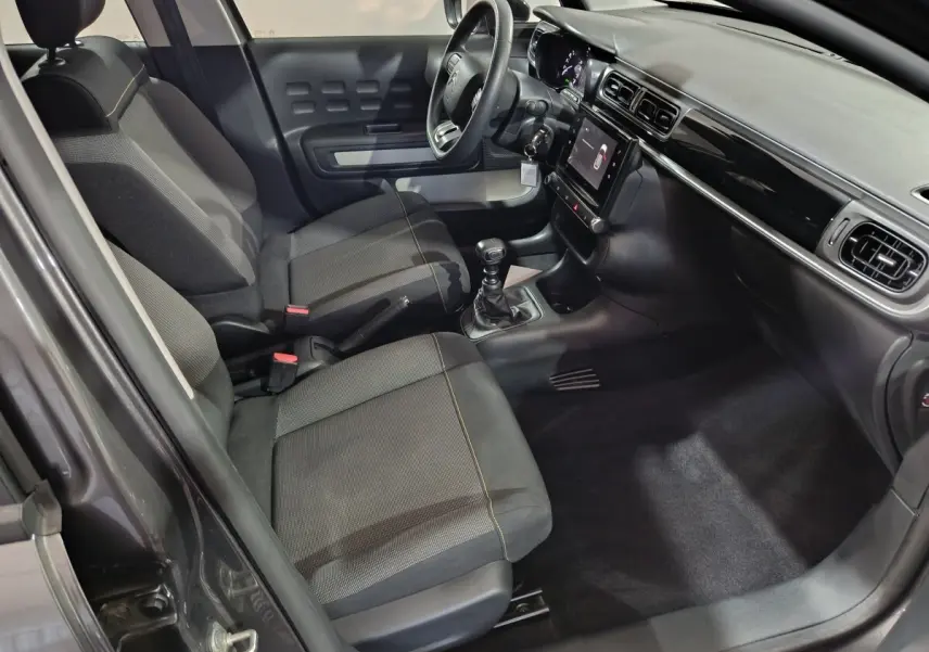 Intérieur avant droit de la Citroën C3 2024 gris foncé, volant multifonctions, écran tactile central et boîte manuelle.