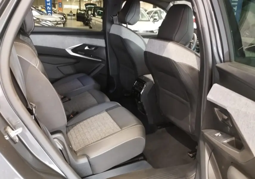Vue intérieure arrière côté gauche du Peugeot 5008 gris titanium, mettant en valeur les sièges tissu et cuir avec surpiqûres blanches.