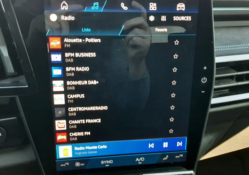 Écran tactile central du Renault Austral E-Tech hybride 2025 affichant la liste des radios, intérieur noir avec surpiqûres bleues.
