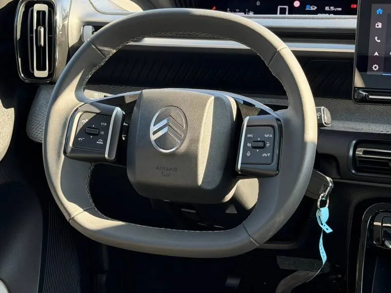 Vue rapprochée du volant gris clair du Citroën C3 2025 avec commandes intégrées et tableau de bord numérique.