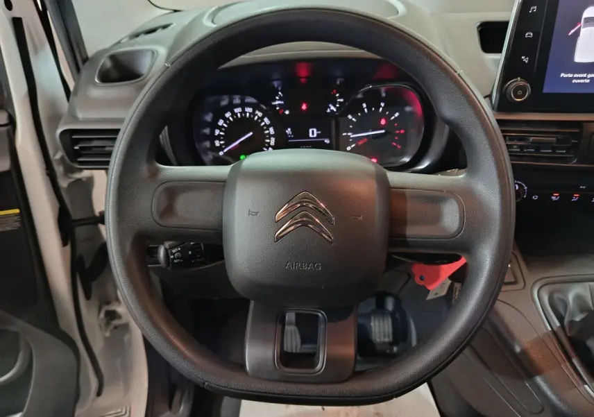 Vue rapprochée du volant noir avec logo Citroën et tableau de bord éclairé du Berlingo blanc 2021.