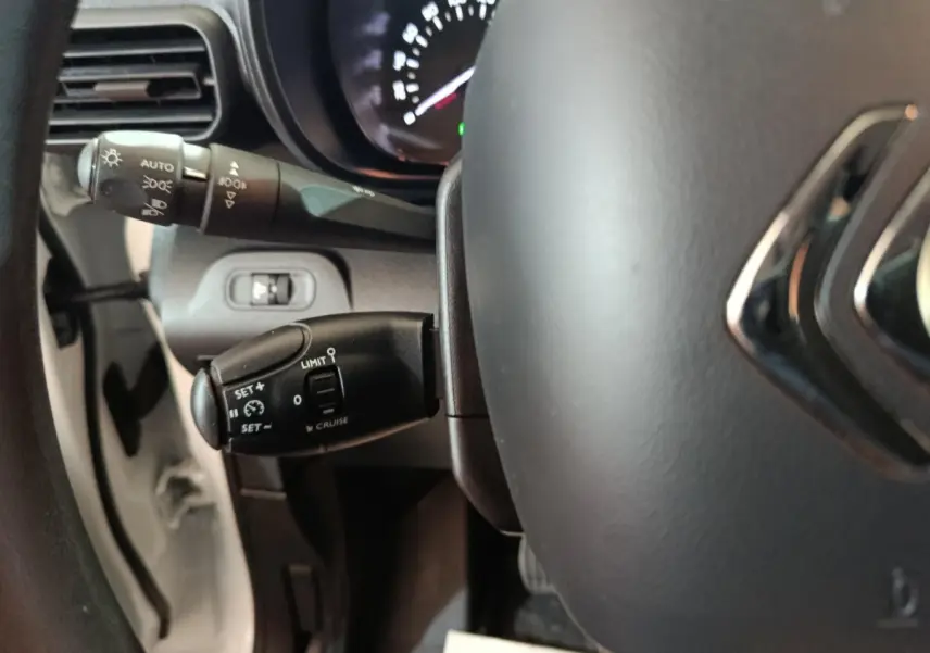 Vue rapprochée du volant et des commandes de régulateur de vitesse du Citroën Berlingo blanc, côté gauche.