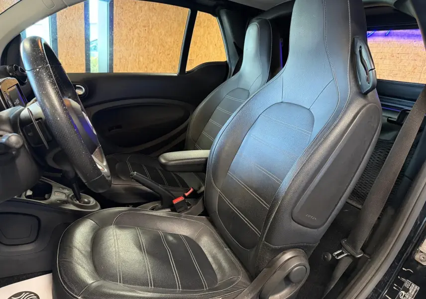 Vue intérieure côté conducteur de la Smart Fortwo Cabrio noire 2019, sièges semi-cuir et volant multifonctions visibles.