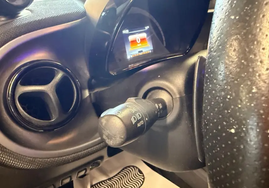 Gros plan sur la commande des phares et le tableau de bord numérique d'une Smart Fortwo Cabrio noir, intérieur semi-cuir.