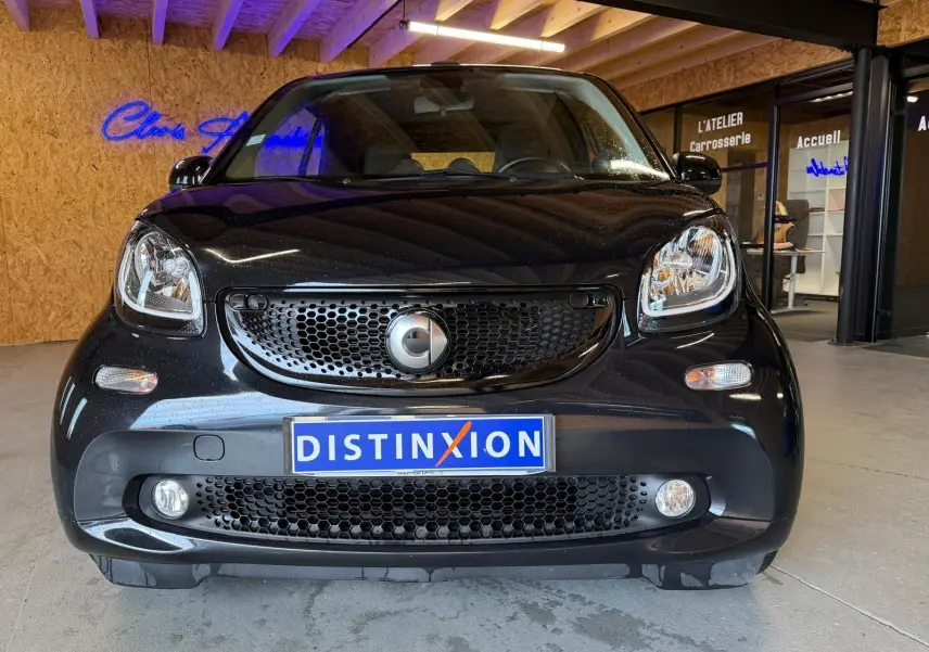 Vue frontale d'une Smart Fortwo Cabrio noire 2019 avec calandre noire et phares arrondis, en intérieur showroom.