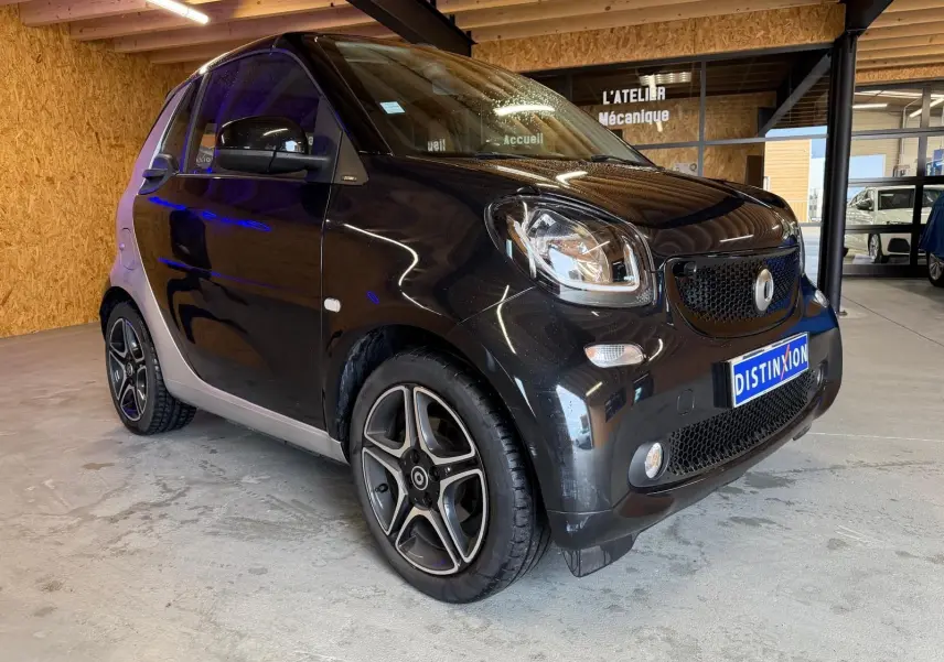Vue 3/4 avant droite d'une Smart Fortwo Cabrio noire avec jantes alu 16'' et toit ouvrant électrique en intérieur showroom.