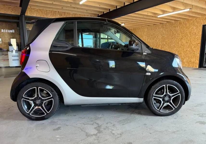 Vue de profil côté gauche d'une Smart Fortwo Cabrio noire avec toit ouvert et jantes alu 16 pouces bicolores.