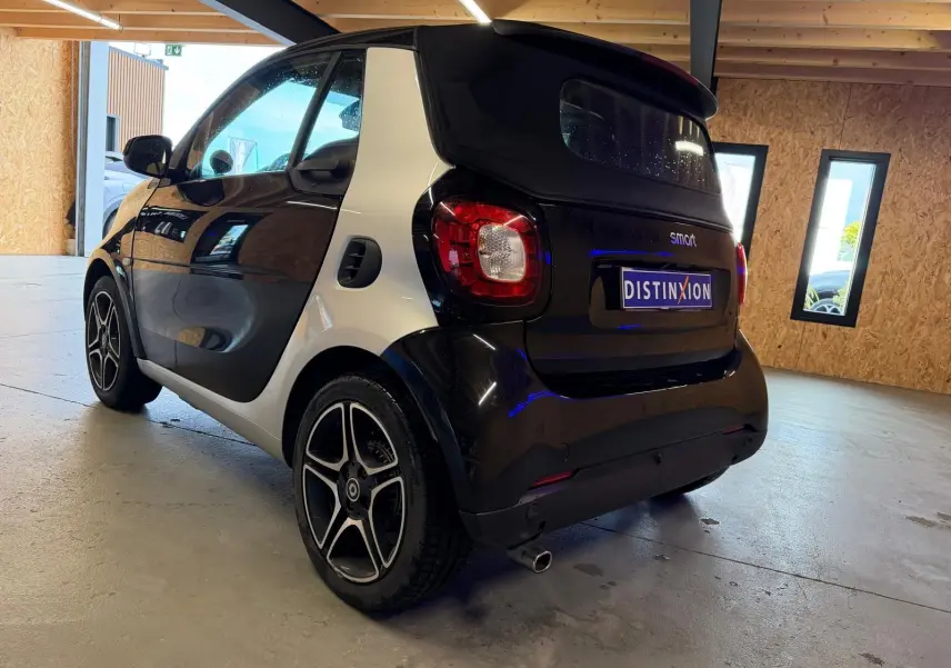 Vue 3/4 arrière droite d'une Smart Fortwo Cabrio noire avec jantes alu 16'' dans un garage lumineux.