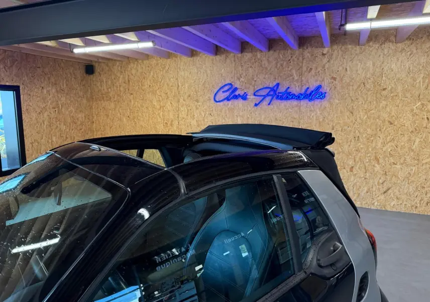Vue 3/4 arrière droite d'une Smart Fortwo Cabrio noire avec toit ouvrant électrique partiellement ouvert en intérieur showroom.