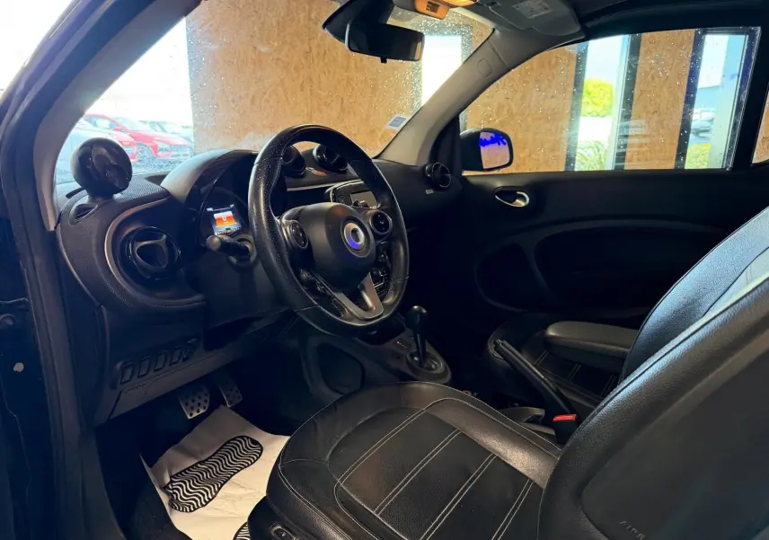 Vue intérieure côté conducteur de la Smart Fortwo Cabrio noire, montrant le volant multifonctions et les sièges semi-cuir.