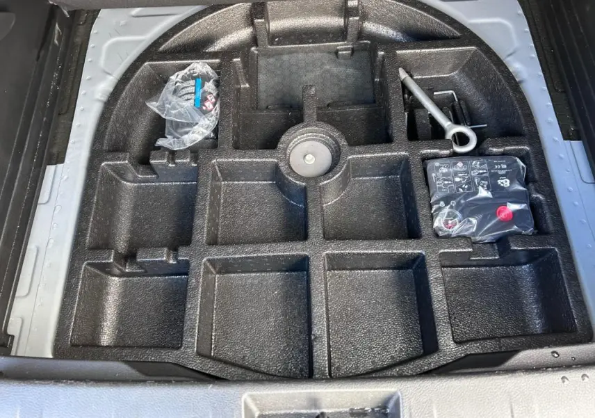 Vue plongeante sur le rangement noir sous le coffre du Jeep Renegade bleu foncé, avec outils et compresseur visibles.