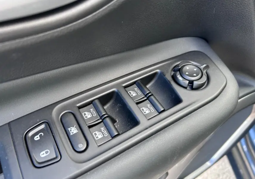 Gros plan sur les commandes de vitres électriques et rétroviseurs sur la porte côté conducteur du Jeep Renegade bleu foncé.